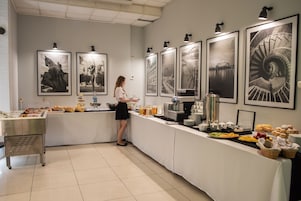 Montaje de bufé con diversos alimentos y bebidas, una máquina de café y fotografías en blanco y negro enmarcadas en la pared.