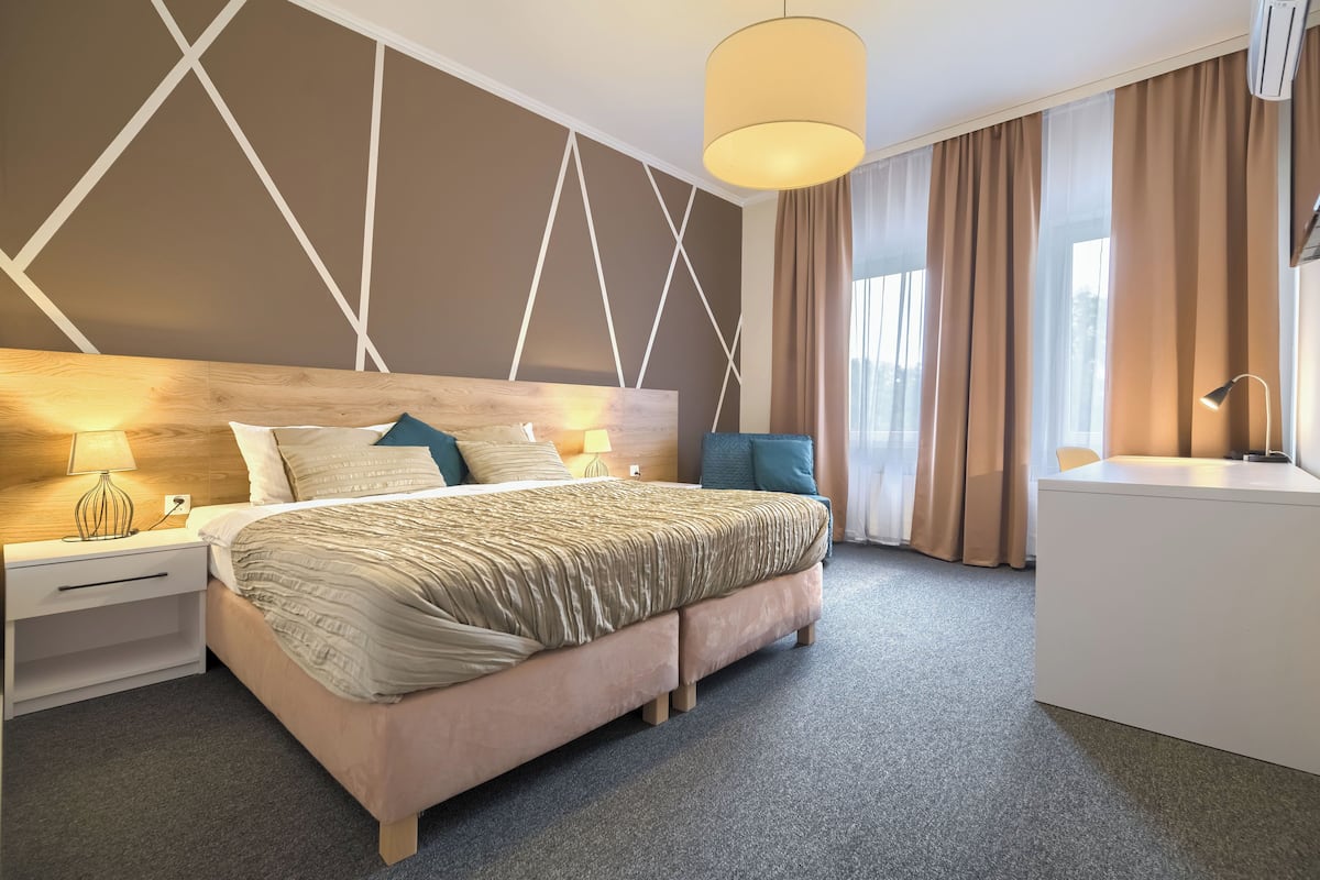 A modern hotel room with a large bed, bedside tables, a desk, and a view of the outdoors.