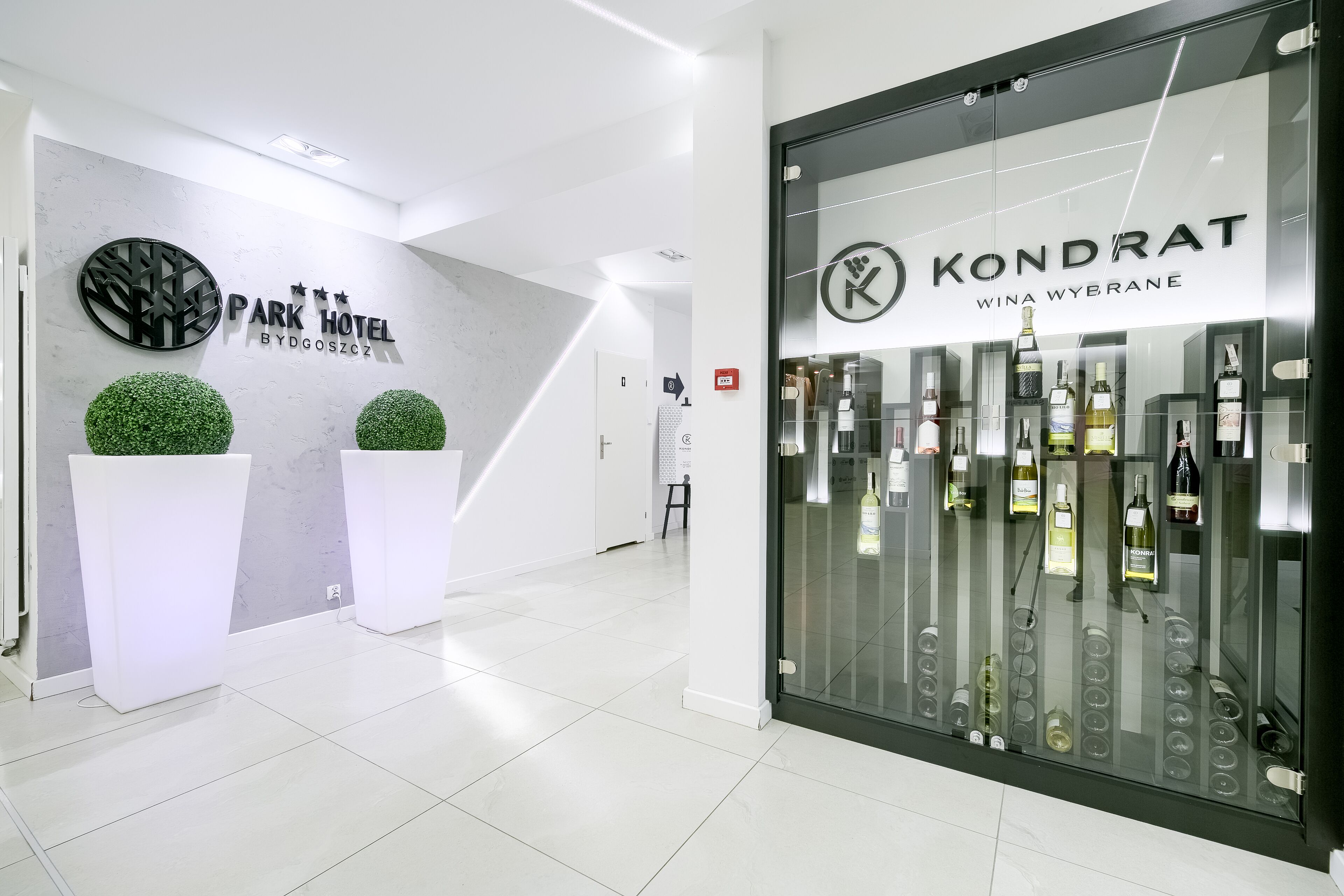 A modern hotel lobby with a reception desk, a glass display of wine bottles, and a sign for 'Park Hotel' and 'Kondrat'.