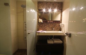 A bathroom with a shower, a sink, a mirror, and a towel rack.