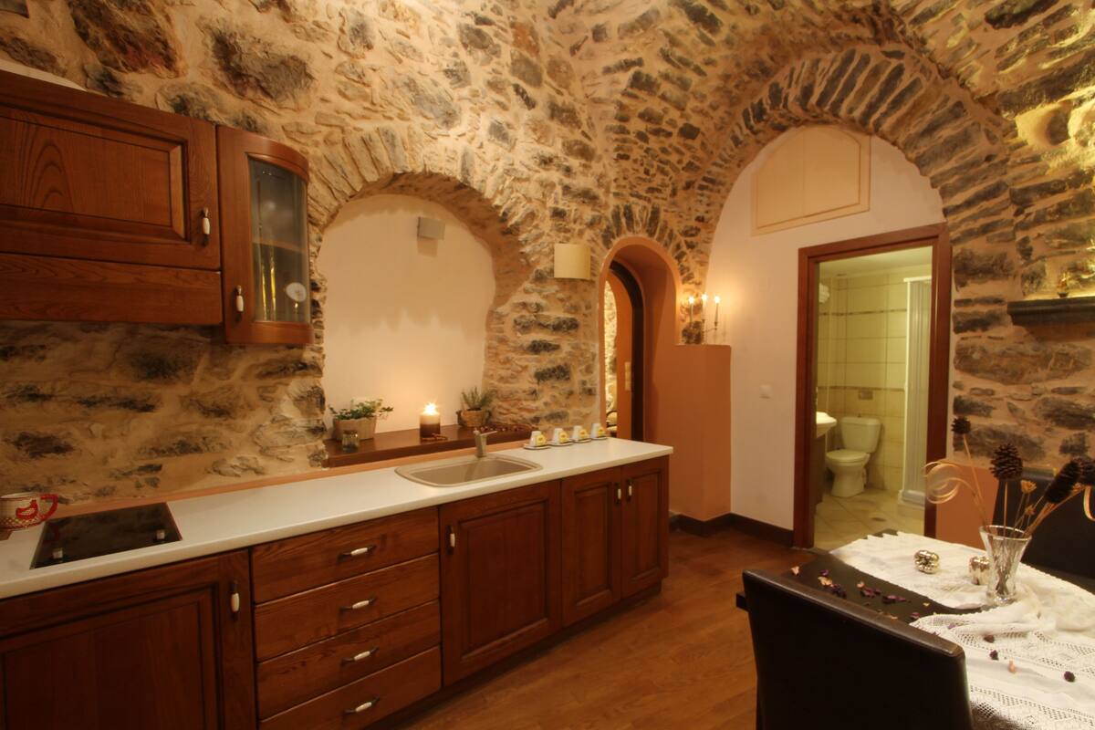 A kitchen with stone walls, wooden cabinets, a sink, and a dining area with a table set for two.