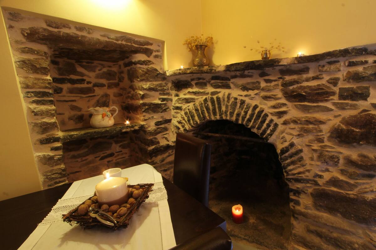 A stone fireplace with a white table in front, a candle, and a vase with dried flowers.