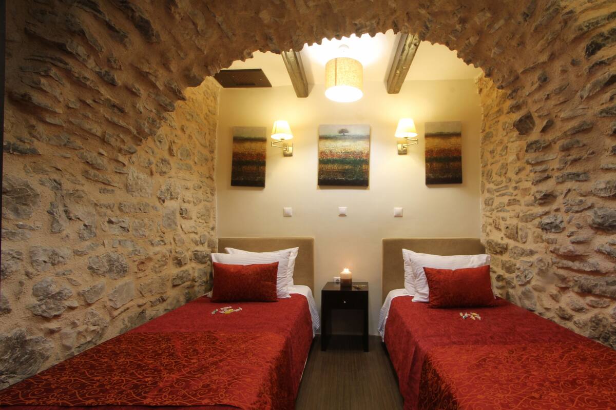 A room with two beds, stone walls, and artwork on the walls.