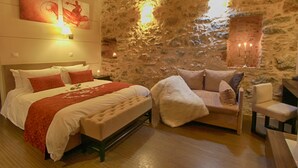 Ein Schlafzimmer mit einer Steinwand, einem Bett mit weißer Bettwäsche und roten Akzenten, einem weißen Sessel und einem hölzernen Nachttisch.