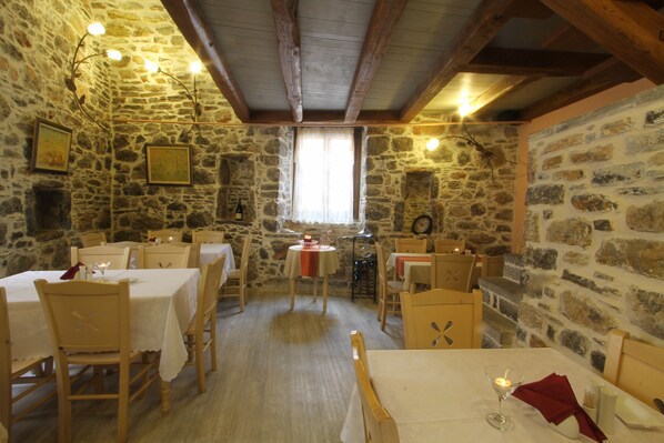 A rustic dining room with stone walls, wooden beams, and tables set for dining.