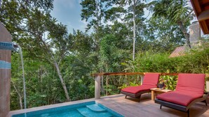 A pool with steps, surrounded by lush greenery and two red cushioned lounge chairs. - Mystic River Resort (San Ignacio)