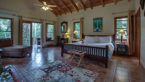 A spacious bedroom with a large bed, wooden ceiling beams, and a ceiling fan. - Mystic River Resort (San Ignacio)
