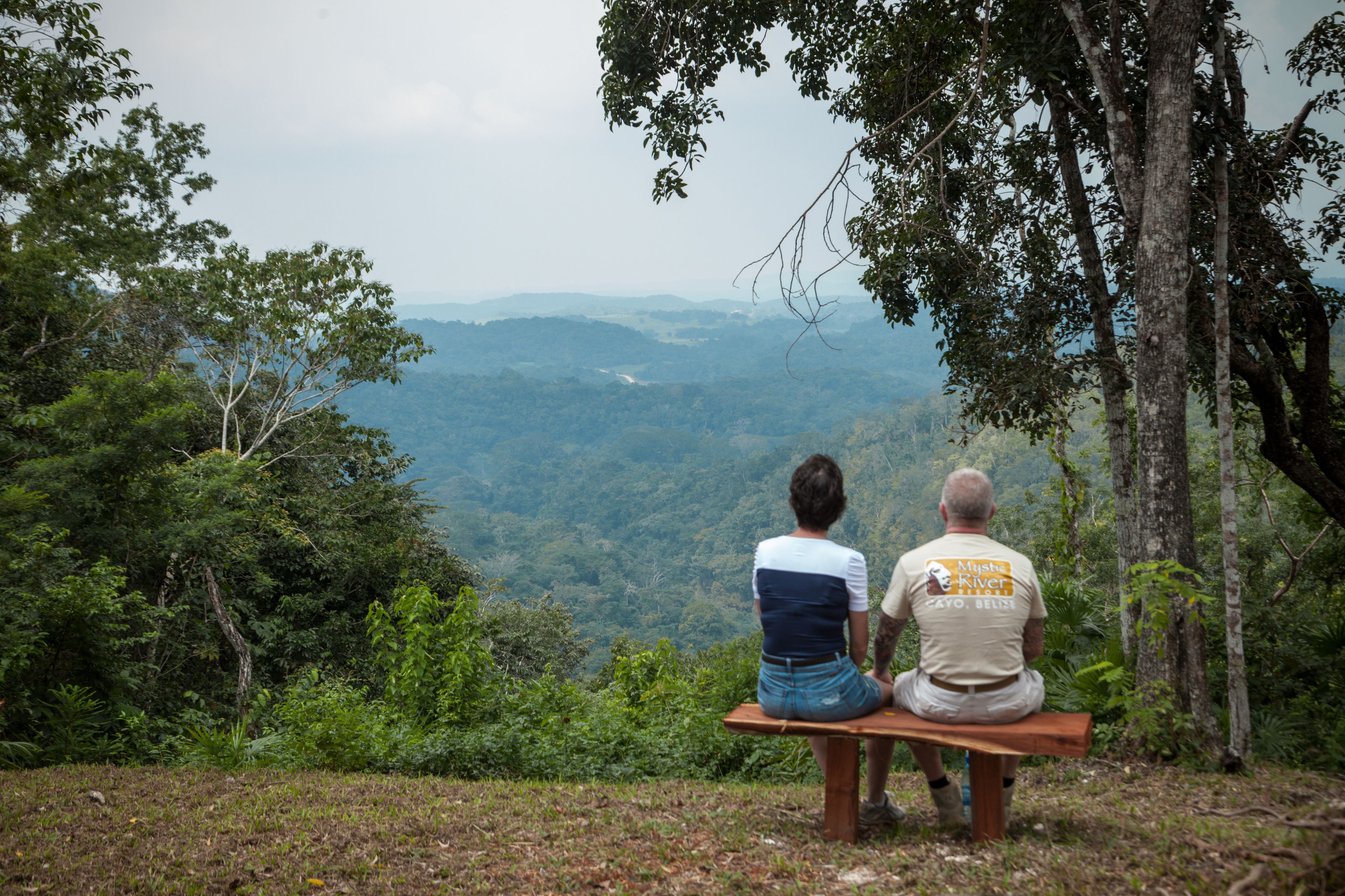 Dos personas sentadas en un banco con vistas a un paisaje montañoso.