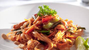 A plate of stir-fried noodles with vegetables and peanuts, garnished with parsley and a lime wedge.