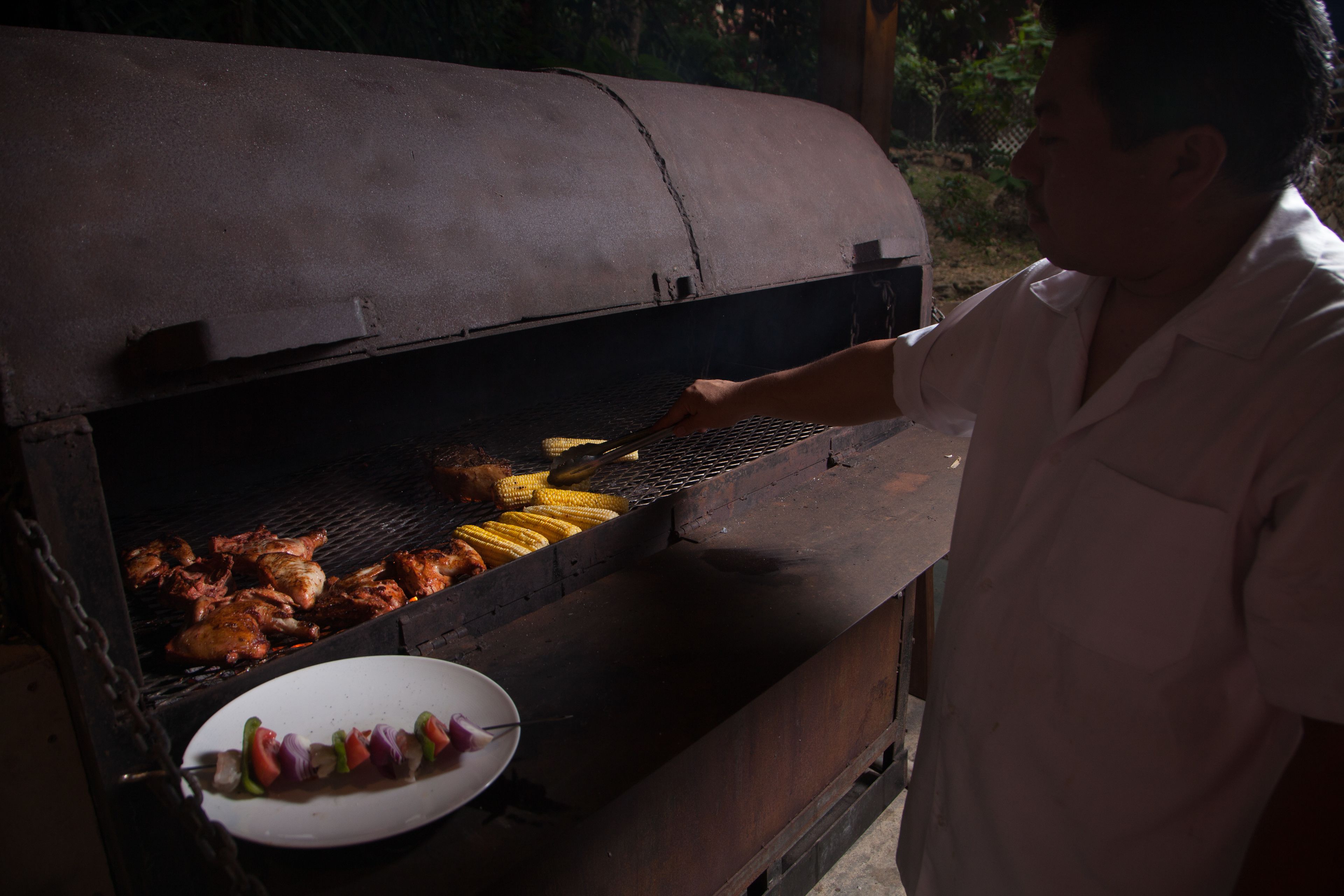 A person grilling chicken and corn on an outdoor barbecue.
