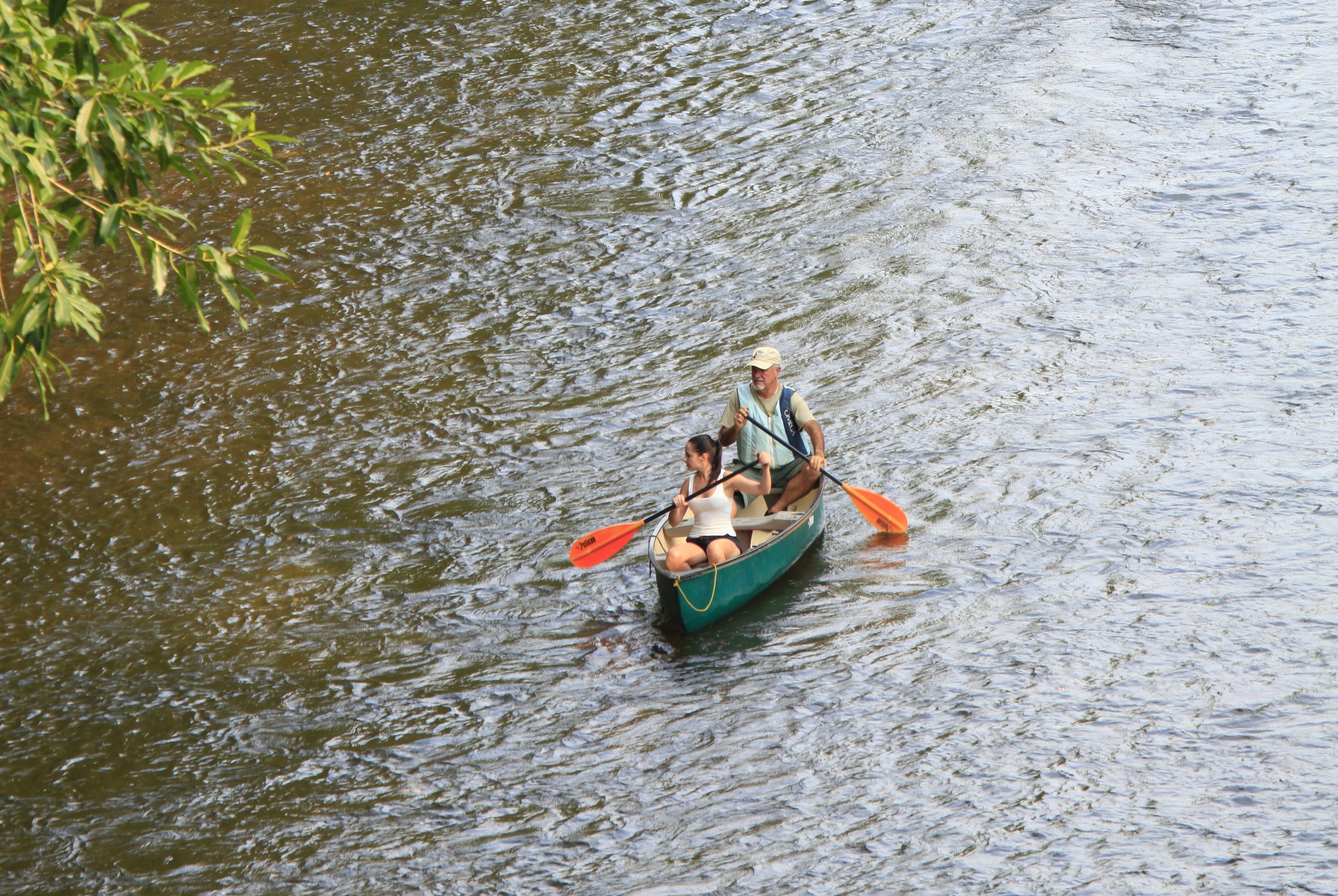 A narrow boat with two people paddling on a river.