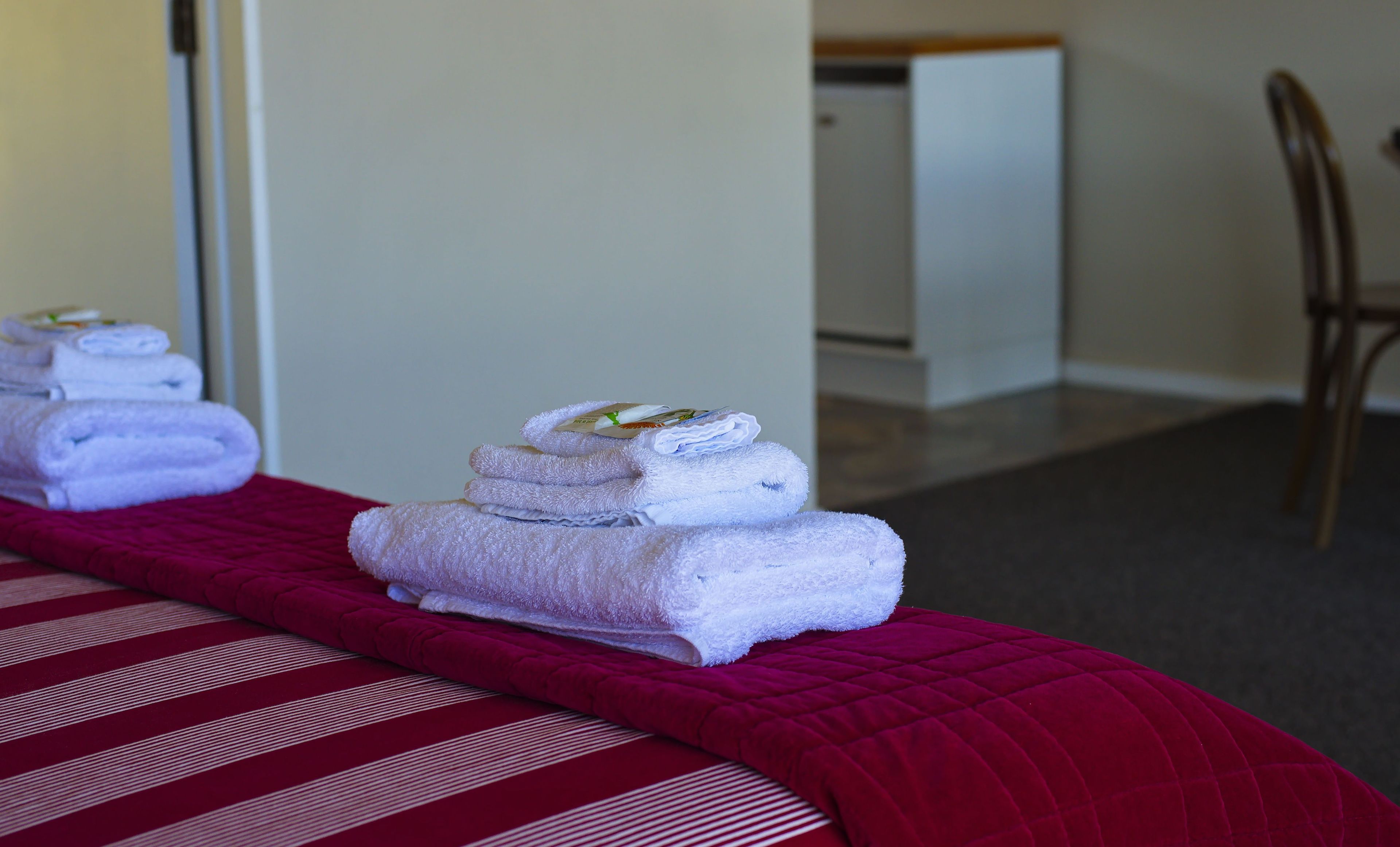 A hotel room with a bed, a red striped bedspread, and two stacks of white towels on a red pillow.