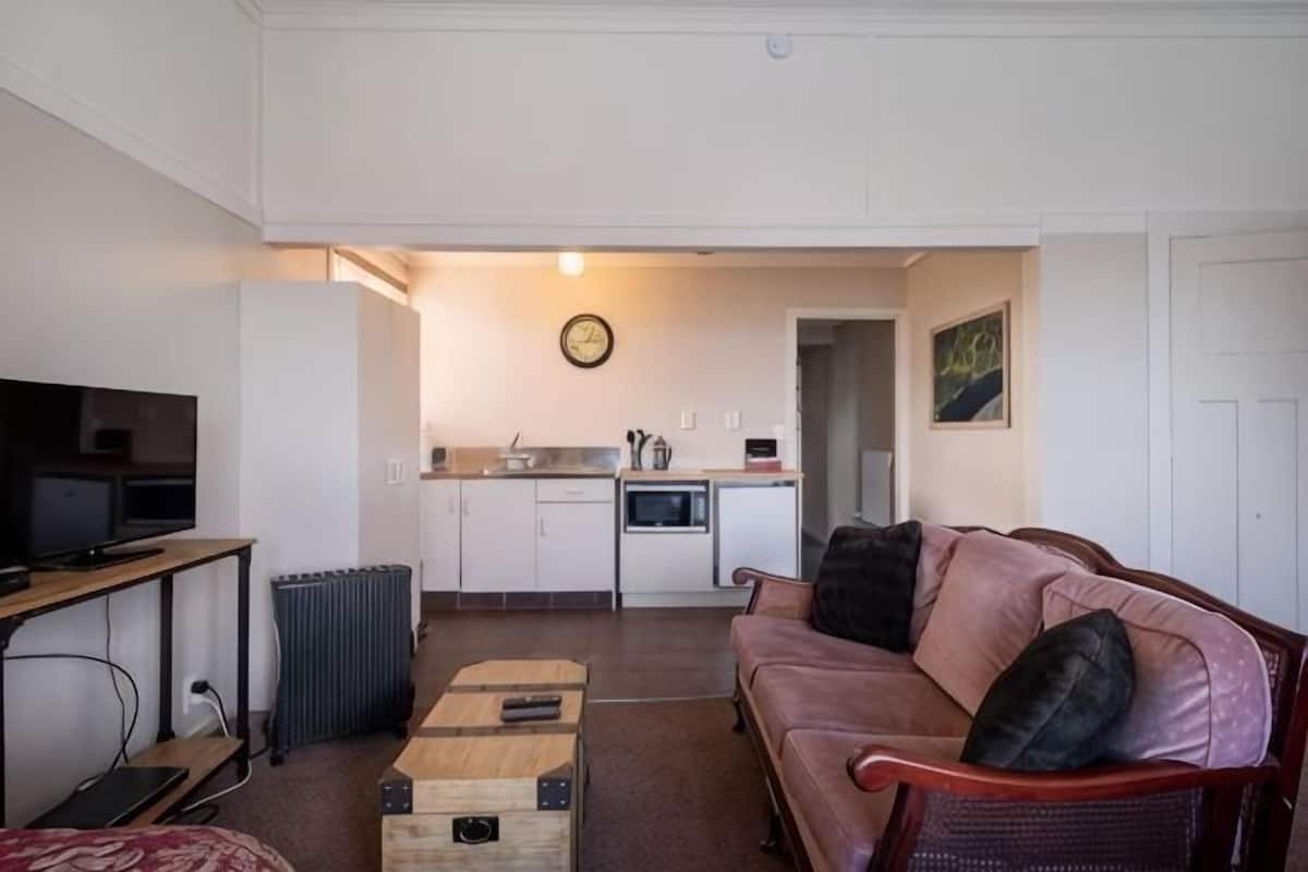 A living room with a television, a sofa, a coffee table, and a kitchen in the background.