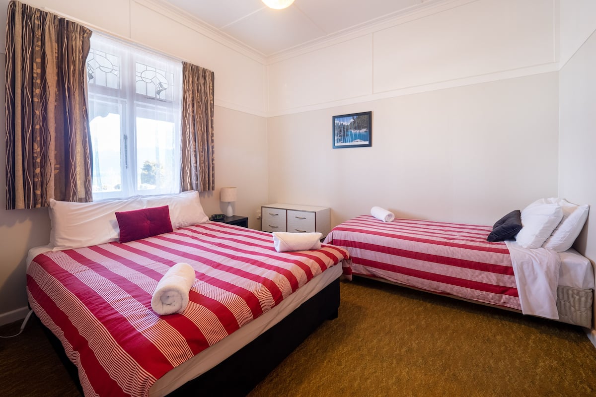 A hotel room with two beds, each with red and white striped bedding, a small bedside table with a lamp, a picture on the wall, and a window with curtains.