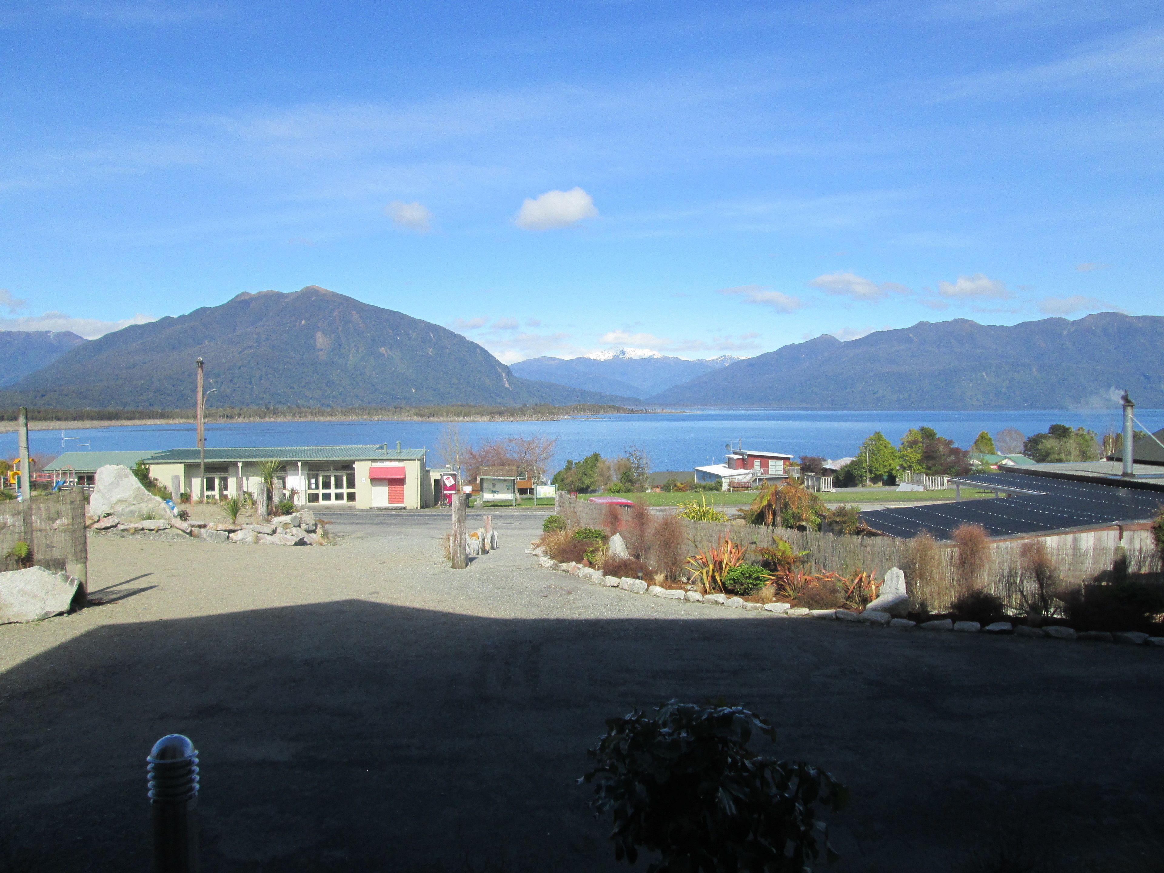 A view of a lakeside property with buildings, a parking area, and mountains in the background.