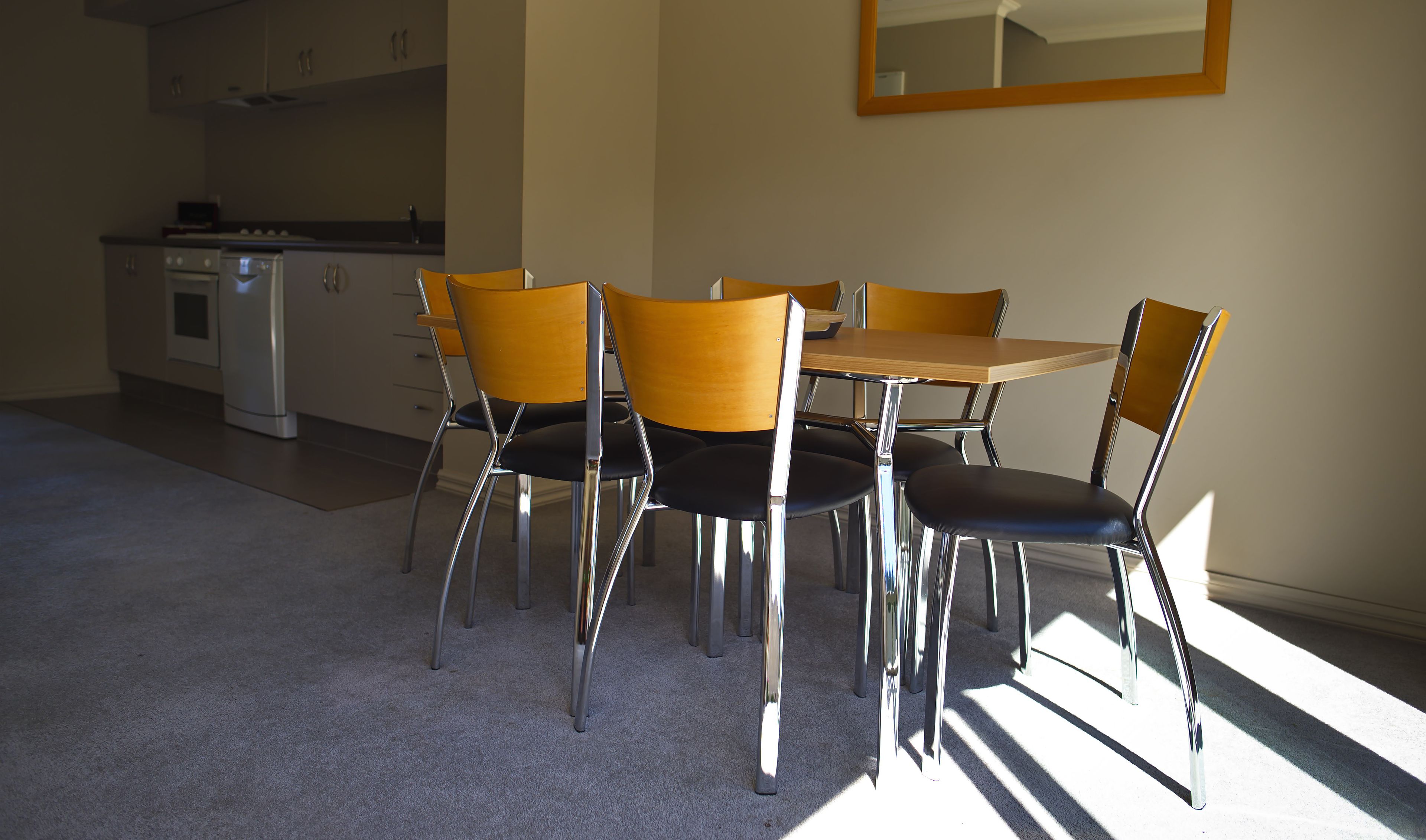 Ein Essbereich mit Tisch und vier Stühlen, eine Küche im Hintergrund und ein Spiegel an der Wand.