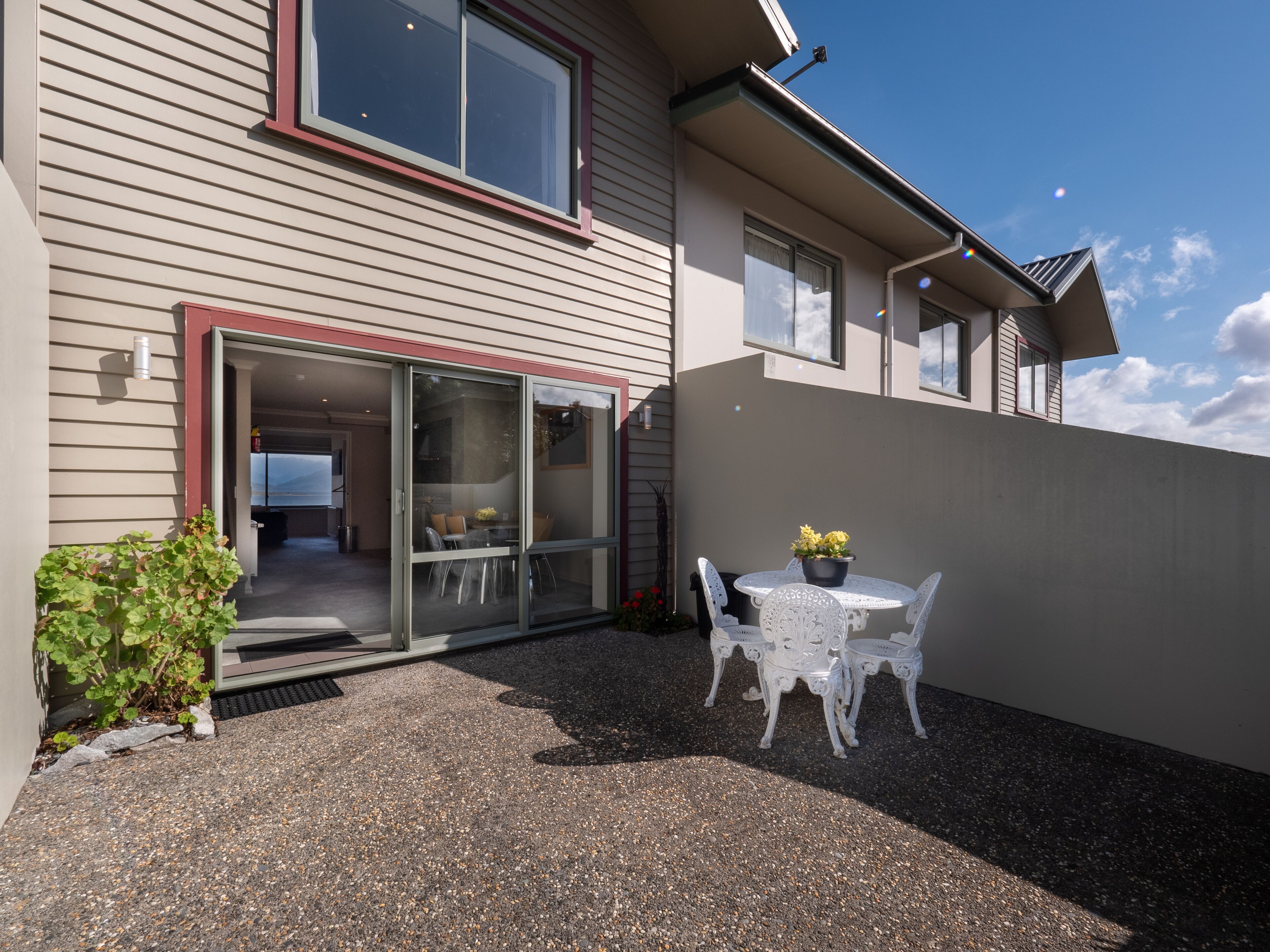 A modern house with a sliding glass door entrance, a patio with a round table and chairs, and a small garden area.