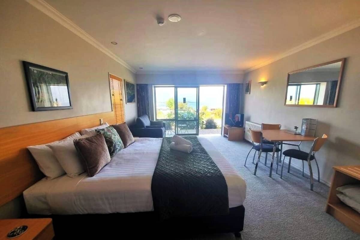 A hotel room with a large bed, a desk, a chair, and a view through the window.