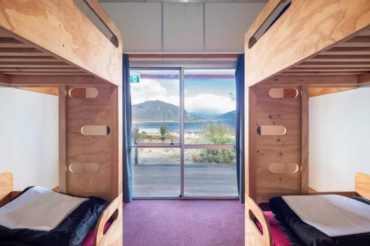 A room with two wooden bunk beds, a large sliding glass door leading to a scenic view, and a purple carpet.
