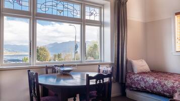 Una habitación con una mesa de comedor y sillas, un sofá, un ventanal con vistas a montañas y un lago, y una cama con cubrecama estampado.