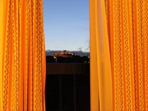 Blick durch Vorhänge auf ein entferntes Gebäude und einen klaren Himmel.