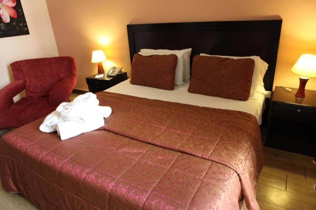 A hotel room with a large bed, two nightstands, a red armchair, and a painting on the wall.
