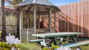 A gazebo with a metal roof and a wooden bench in front. - Blue Mountains Heritage Motel (Katoomba)