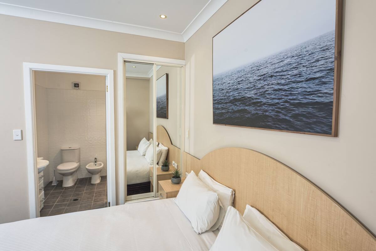 A hotel room with a bed, a bathroom with a toilet and bidet, and a large ocean view.
