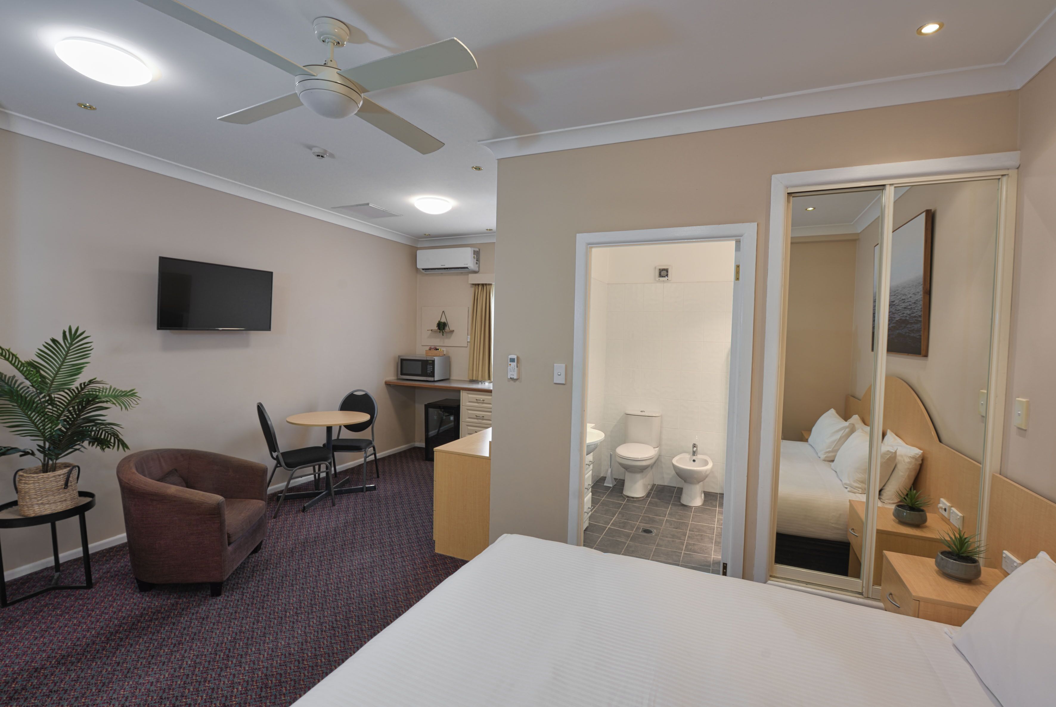 Habitación de hotel con cama, escritorio, silla, televisión y baño visible a través de una puerta abierta.