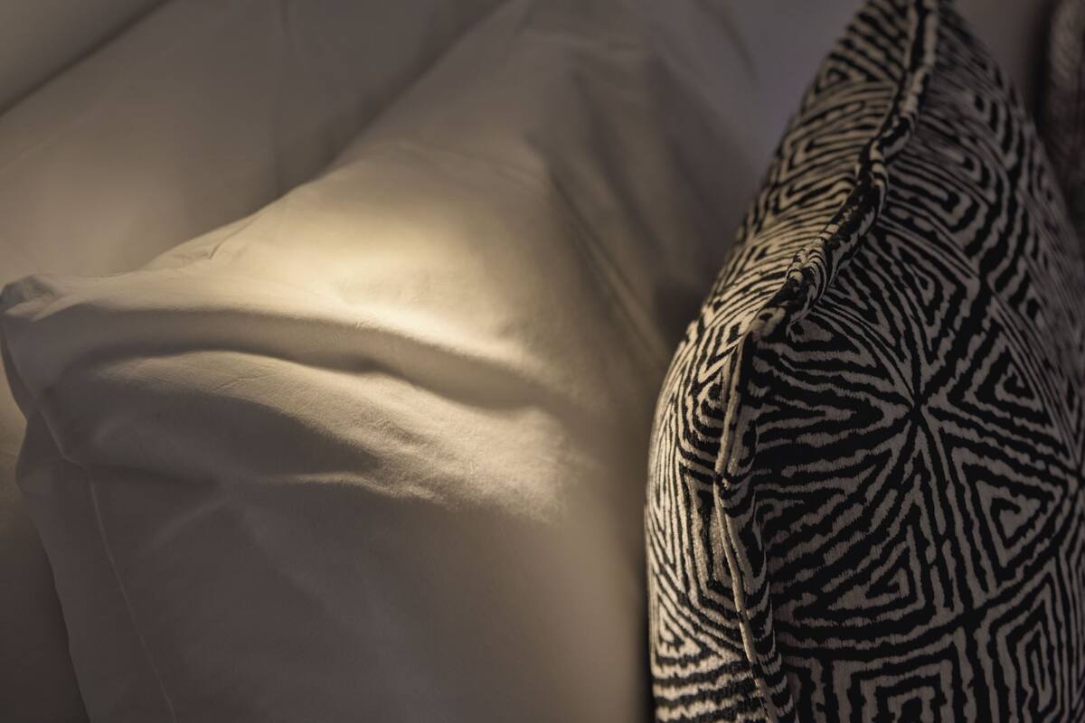 A bed with a headboard, a bedside lamp, and patterned pillows.