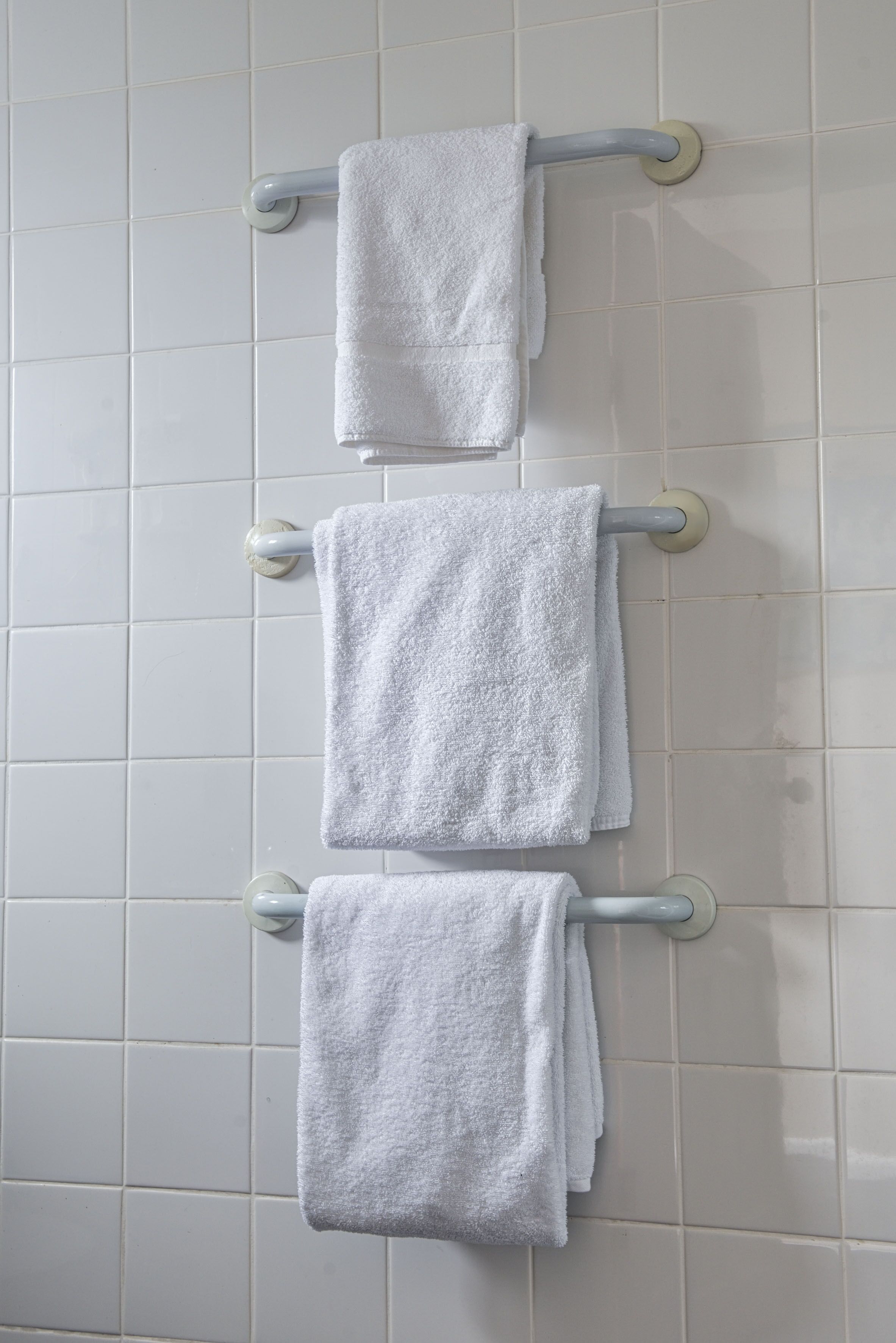 A bathroom with white tiled walls and a towel rack holding three white towels.
