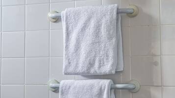 A bathroom with white tiled walls and a towel rack holding three white towels.