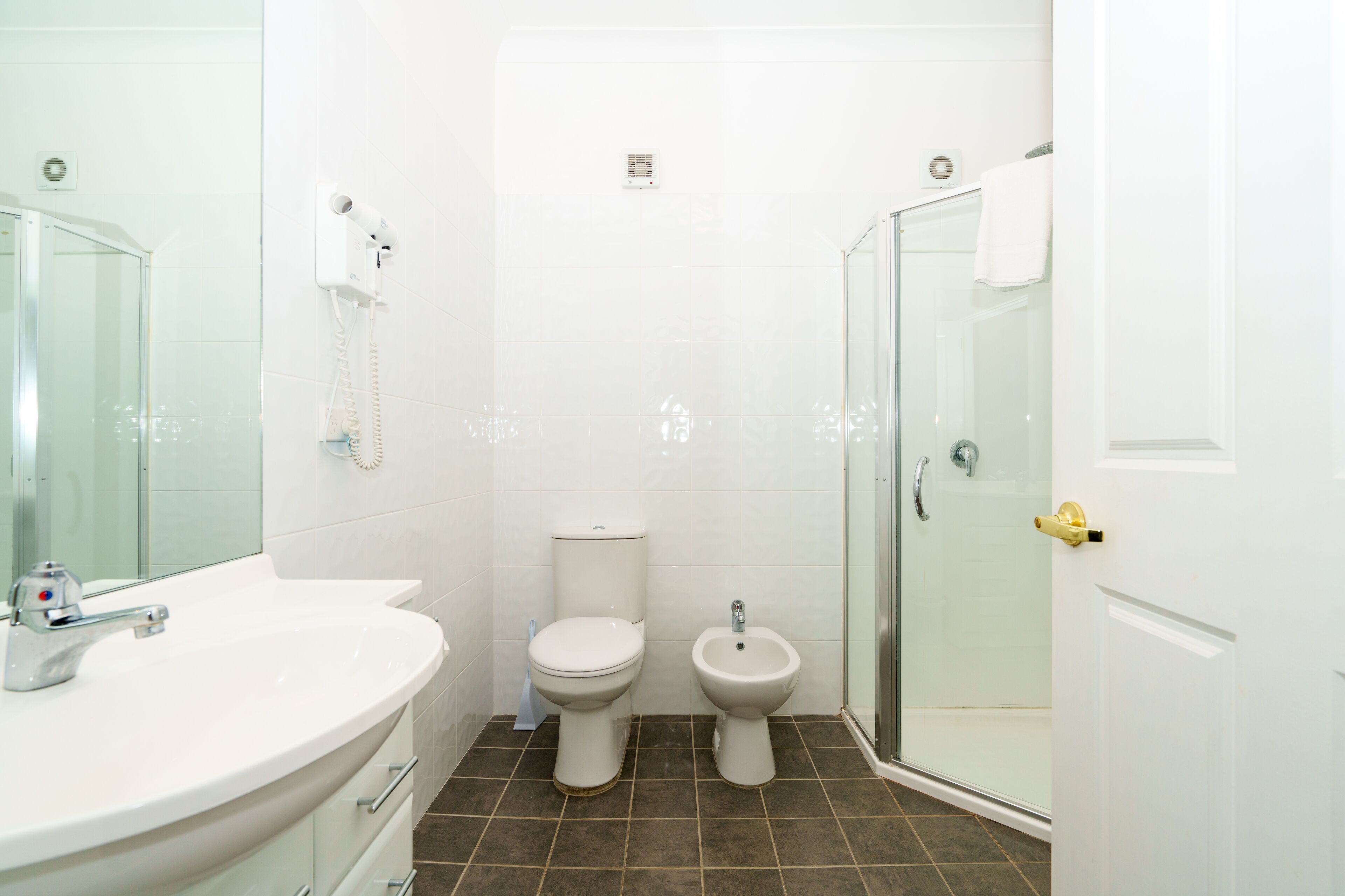 A bathroom with a white sink, toilet, bidet, and glass shower enclosure.