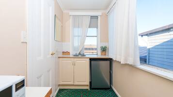 Cozinha compacta com máquina de lavar louça, janela com cortinas e vista para o exterior.