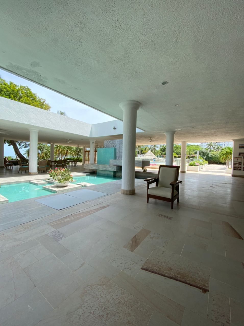 Un espace piscine intérieure avec des fauteuils, des colonnes et une vue sur l’extérieur.