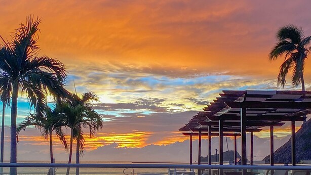 A rooftop terrace with a view of the sunset over the ocean, palm trees, and outdoor seating. - Hotel Tamacá Beach Resort (Santa Marta)