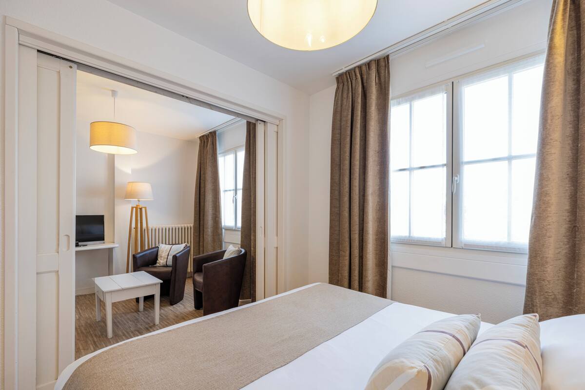 A hotel room with a bed, a desk with a chair, a television, and a lamp.