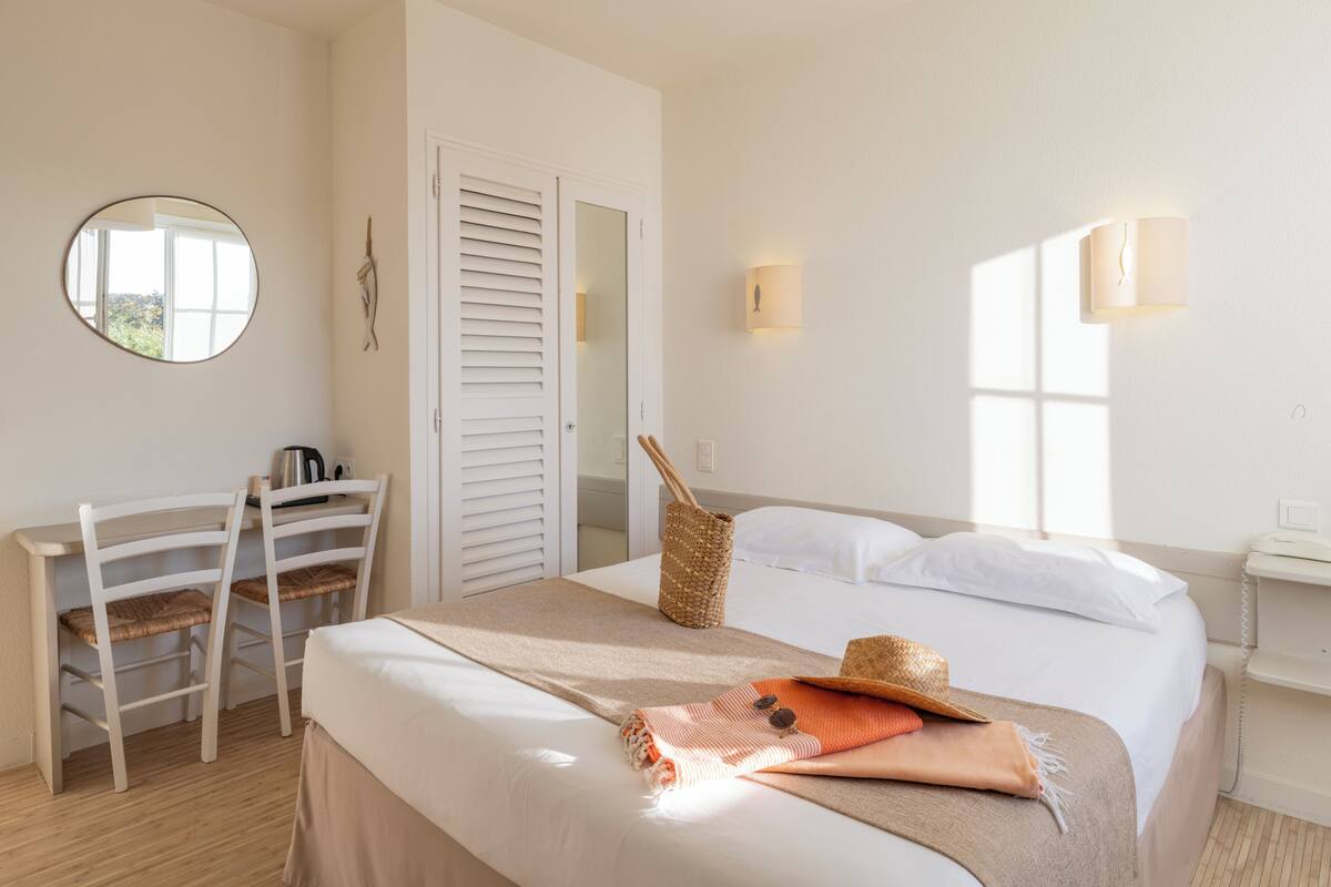 A hotel room with a bed, a desk, a chair, a mirror, and a window.