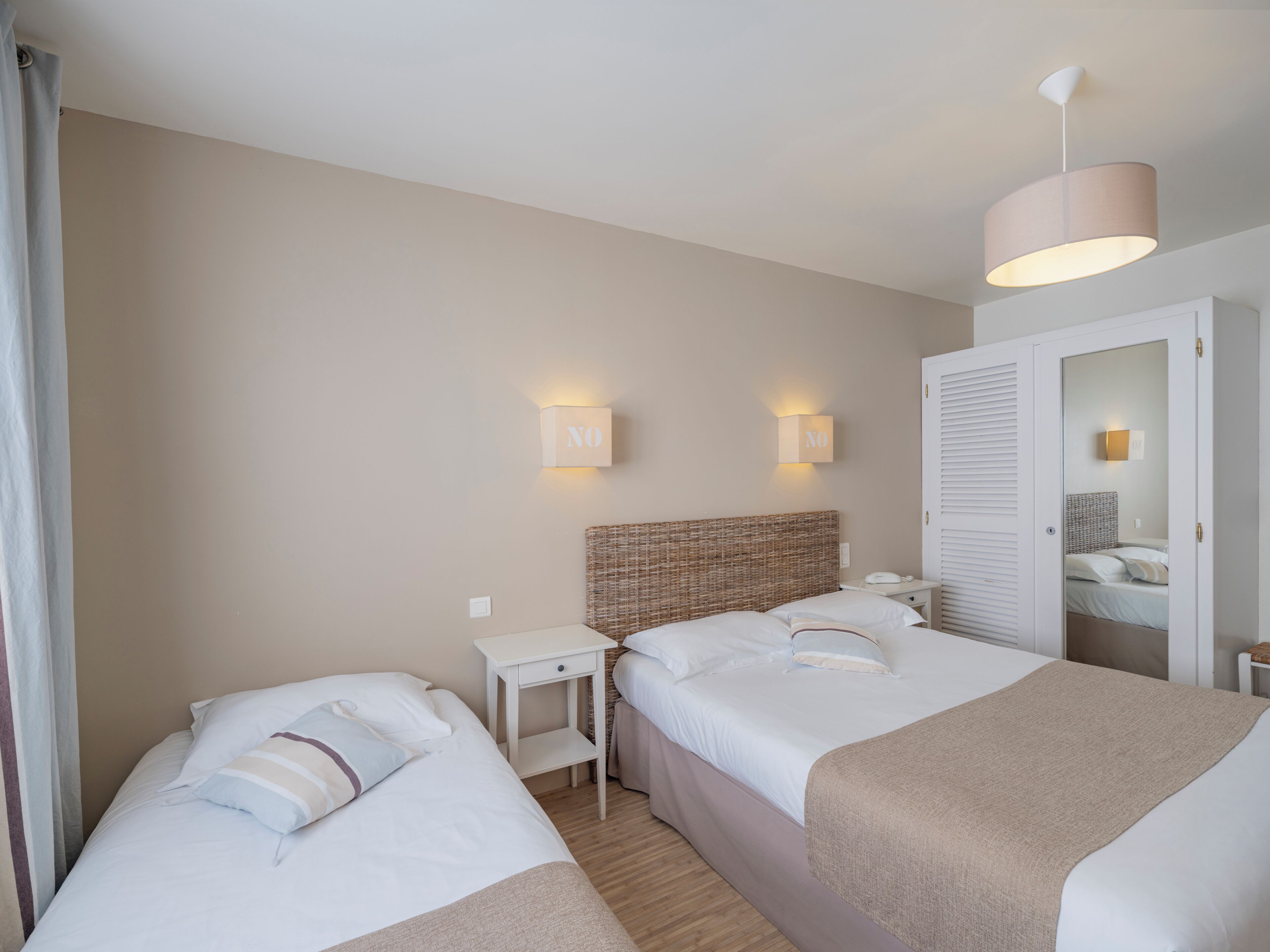A hotel room with two beds, a bedside table, a lamp, and a wardrobe.
