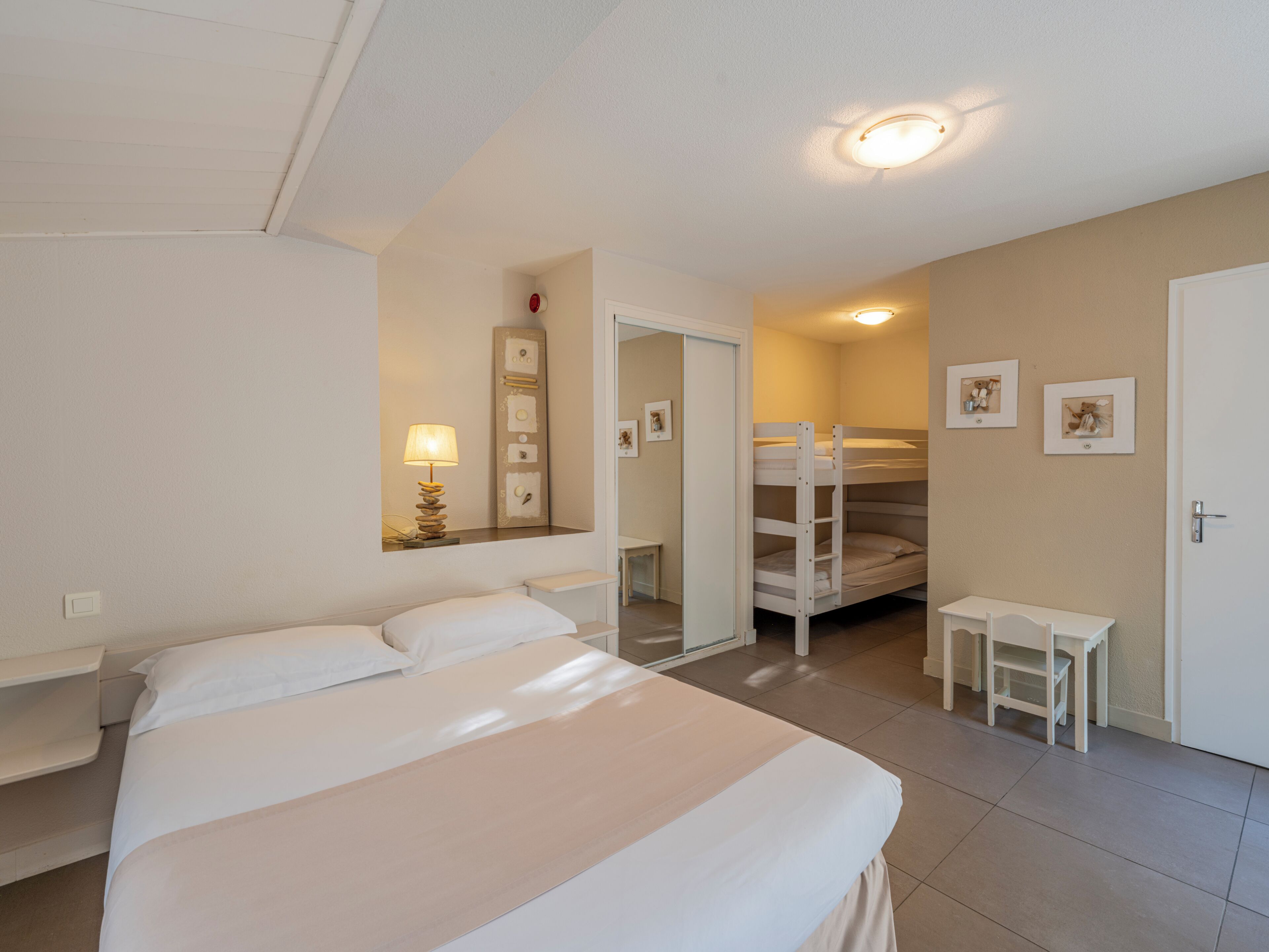 A bedroom with a bed, a desk, a chair, a bunk bed, and a door.