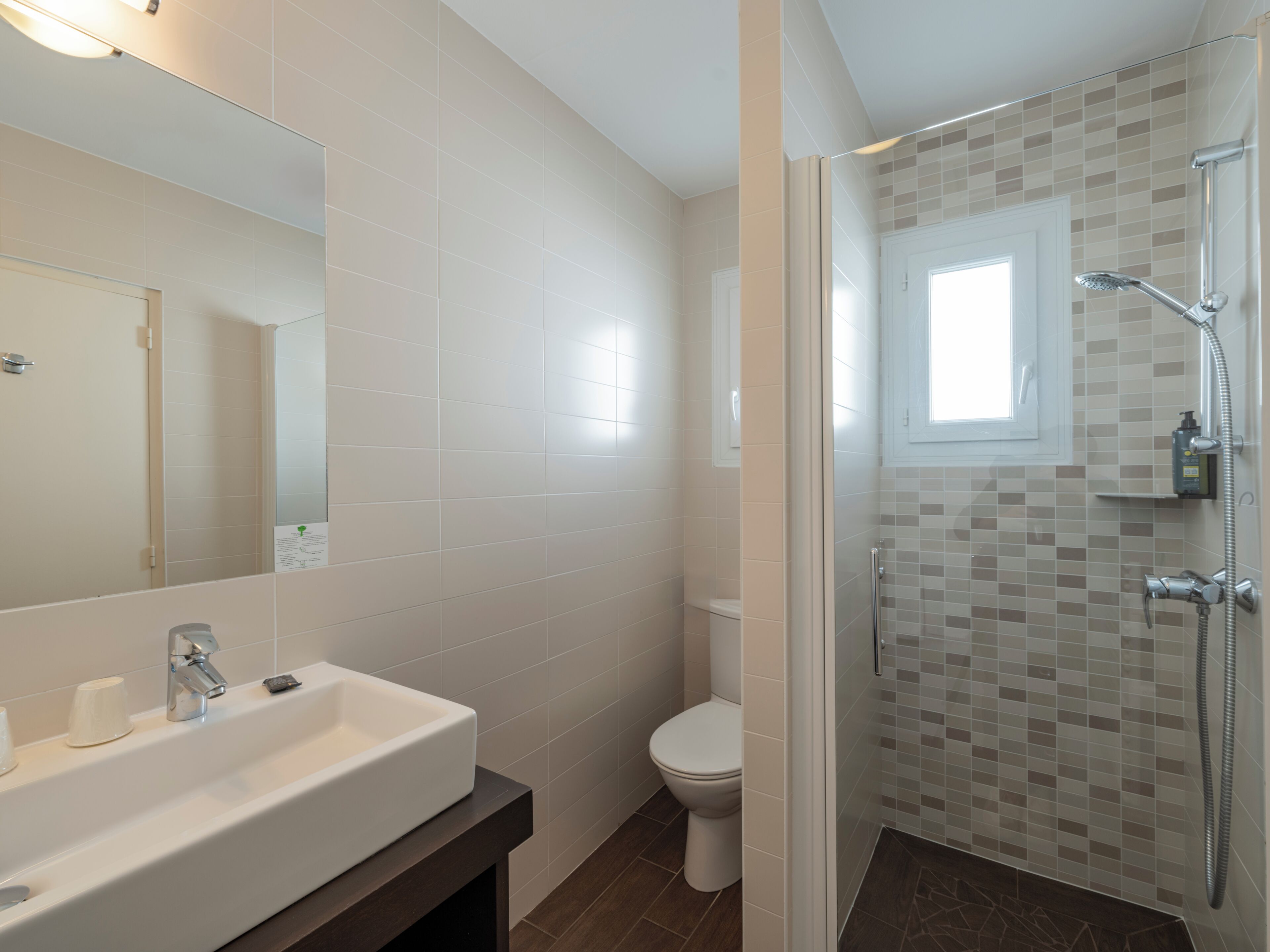 A bathroom with a white sink, a toilet, and a shower area with mosaic tiles.