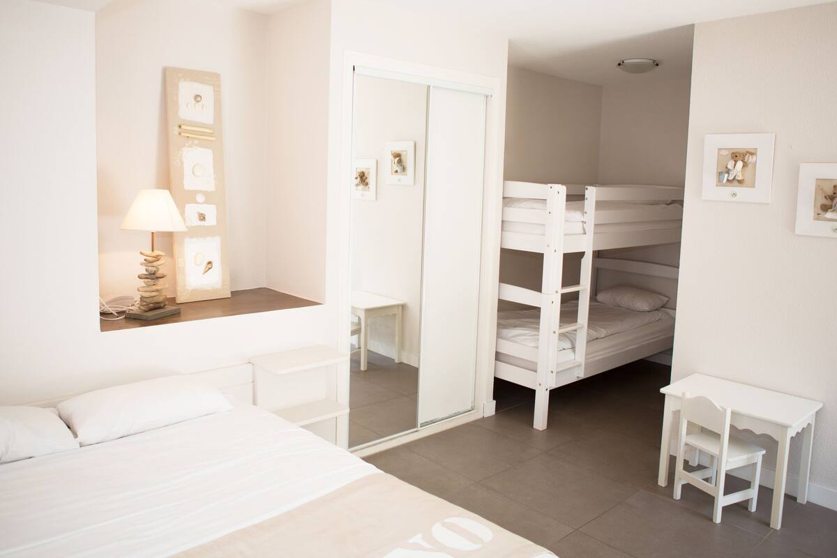 A bedroom with a bunk bed, a bedside table, a lamp, and a mirror.