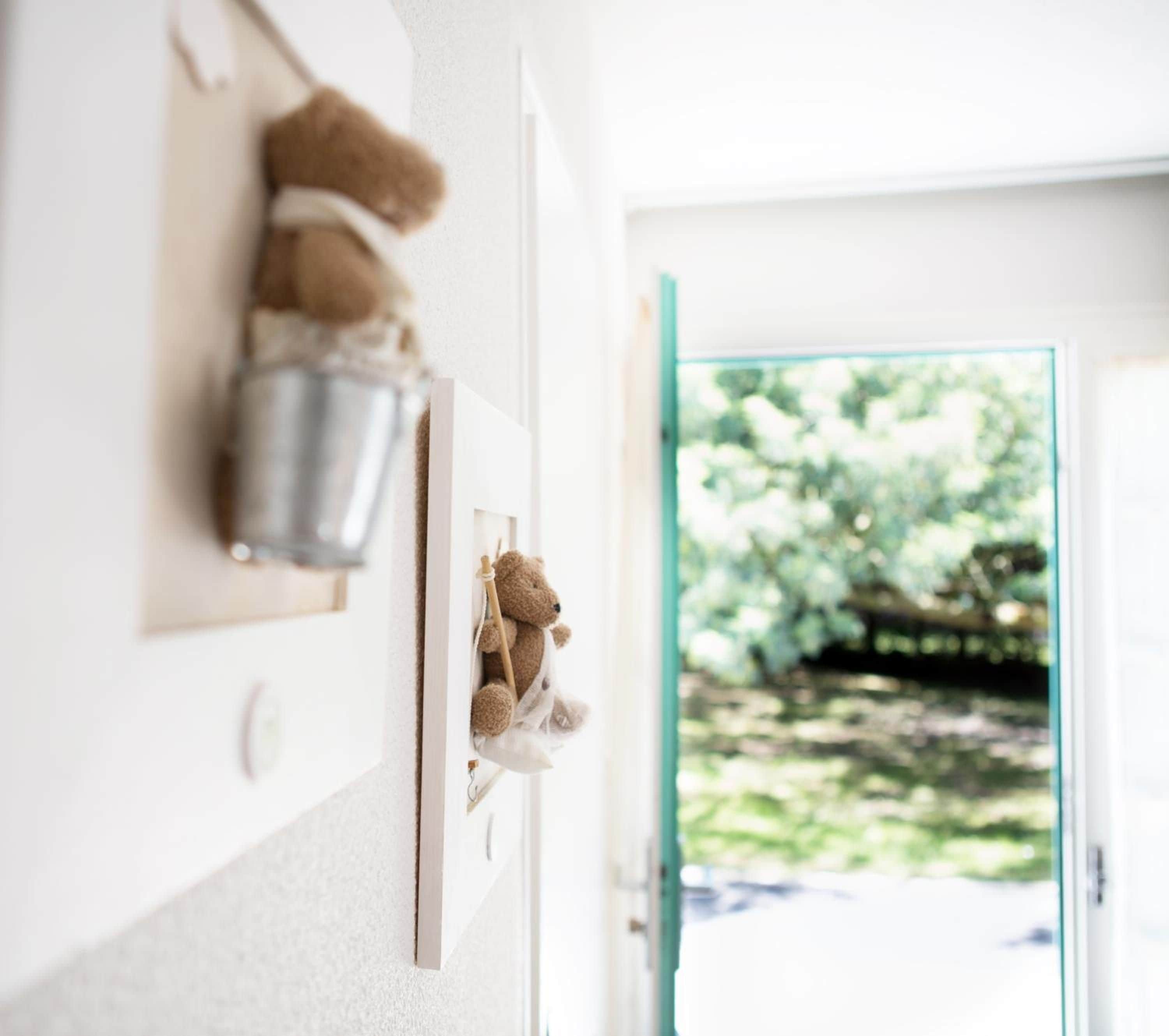 Una puerta con un osito de peluche colgando de un gancho y un pequeño recipiente metálico en la pared.