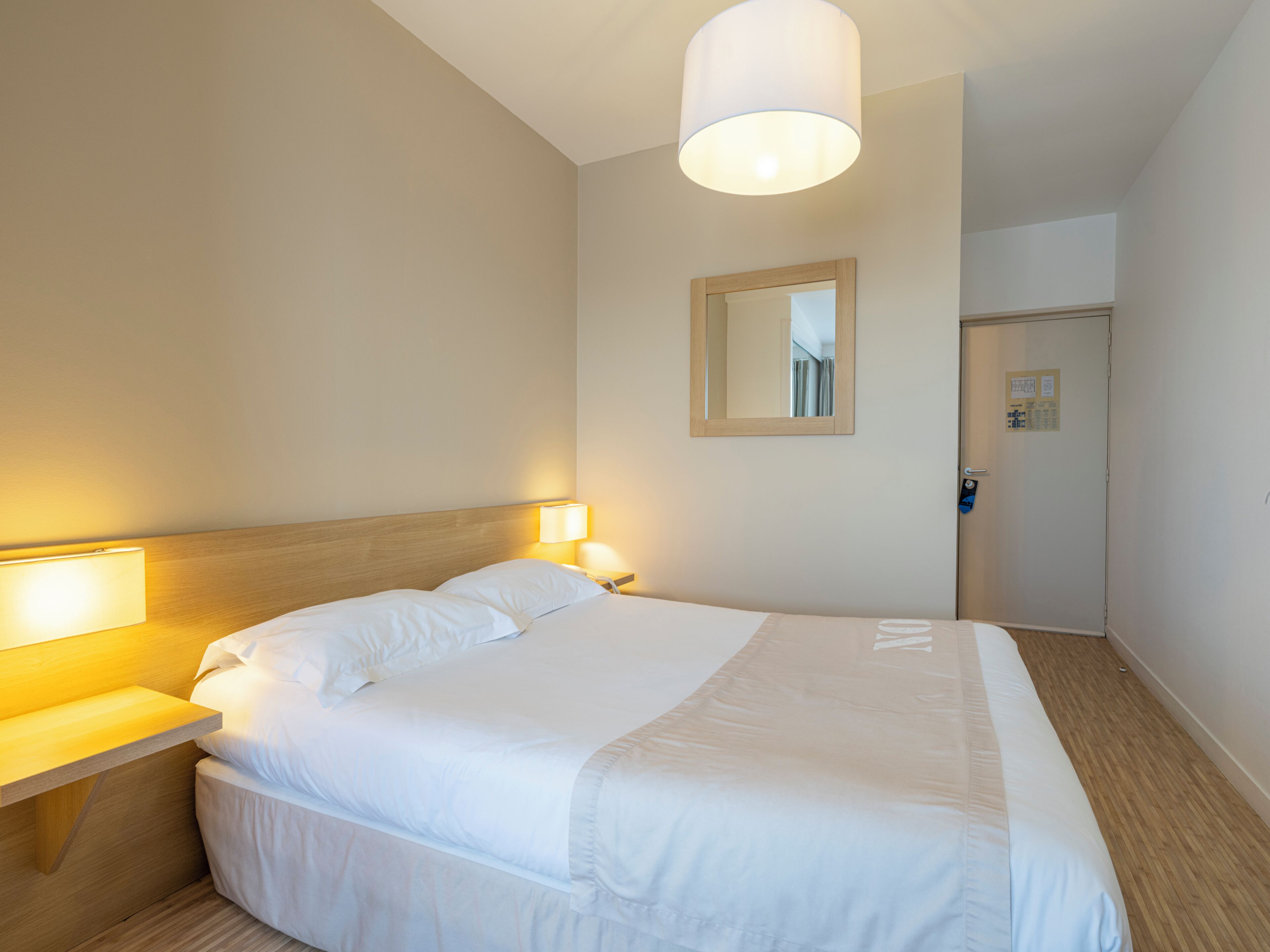 A hotel room with a large bed, bedside lamps, a mirror, and a door with a lock.