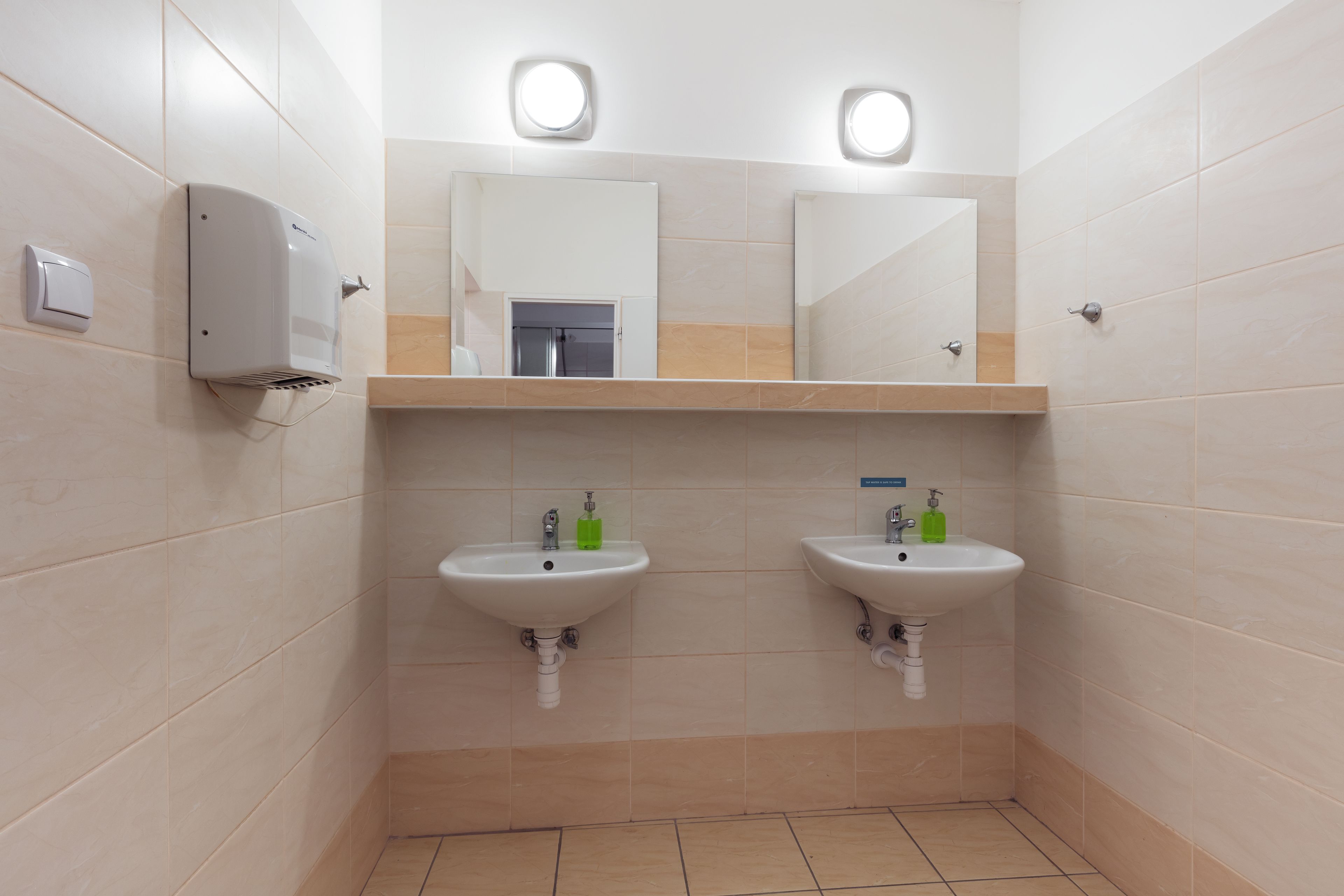 A restroom with two sinks, a hand dryer, and a mirror above each sink.
