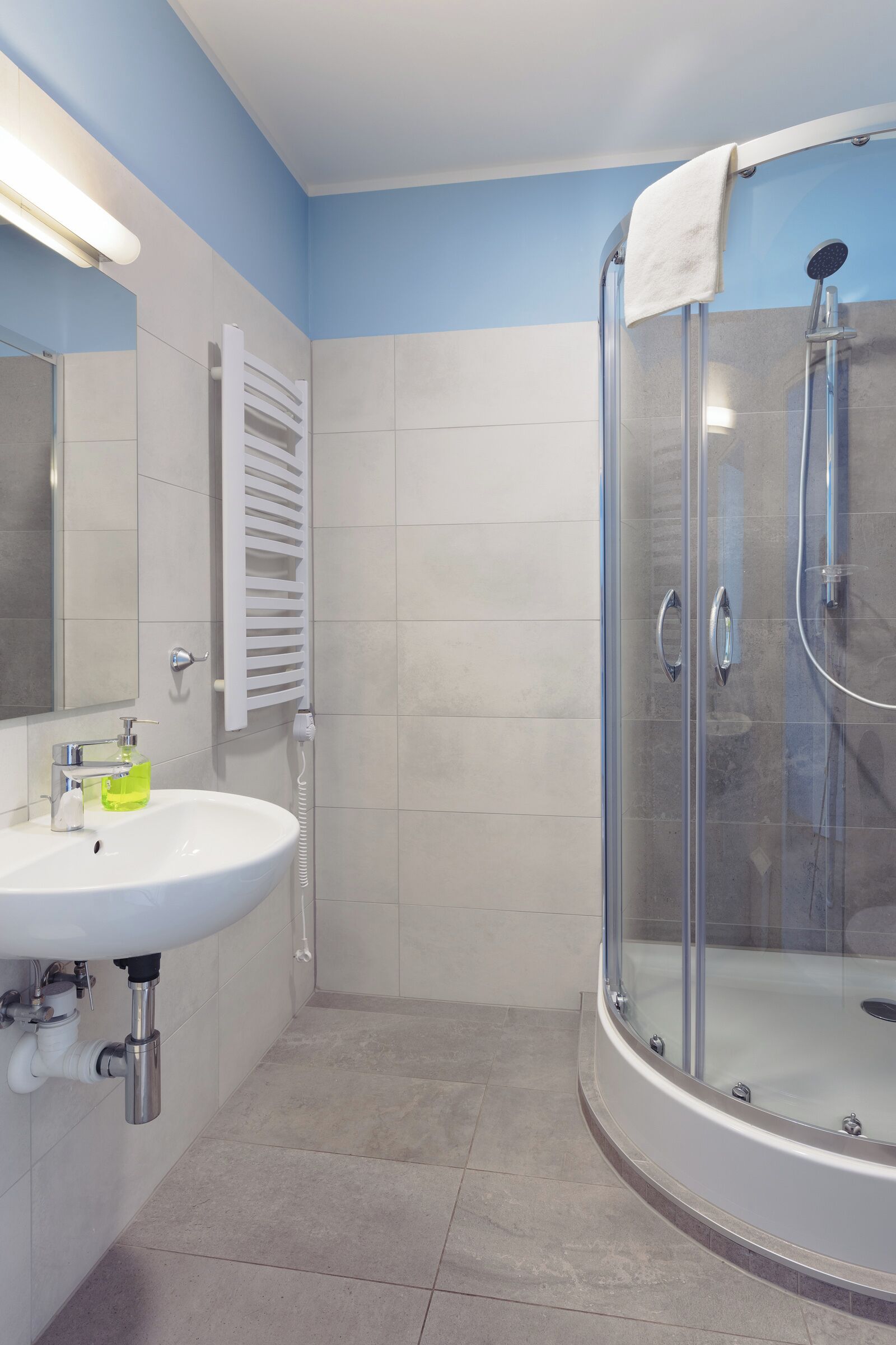 Un baño con ducha de mampara de vidrio, un lavabo blanco con espejo y un perchero para toallas.