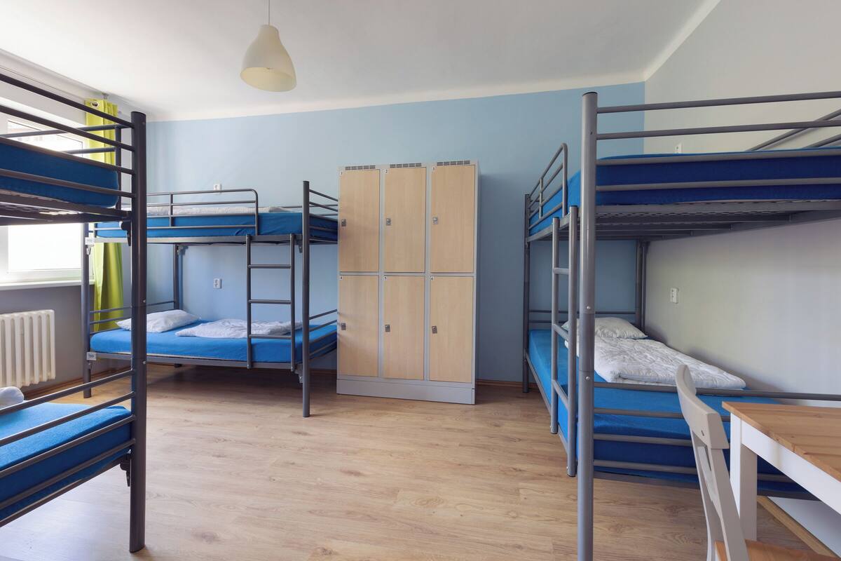 A dormitory room with bunk beds, a wooden wardrobe, and a table with chairs.