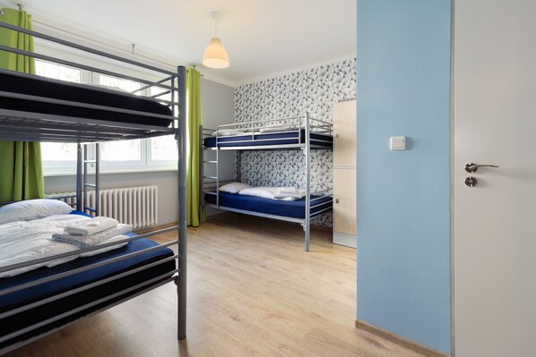 A bunk bed room with a radiator, a window with curtains, and a door. - Patio Hostel (Bratislava)