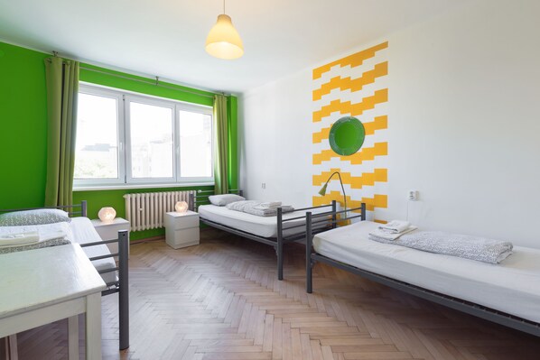 A room with two beds, a table, a radiator, and a window with curtains. - Patio Hostel (Bratislava)