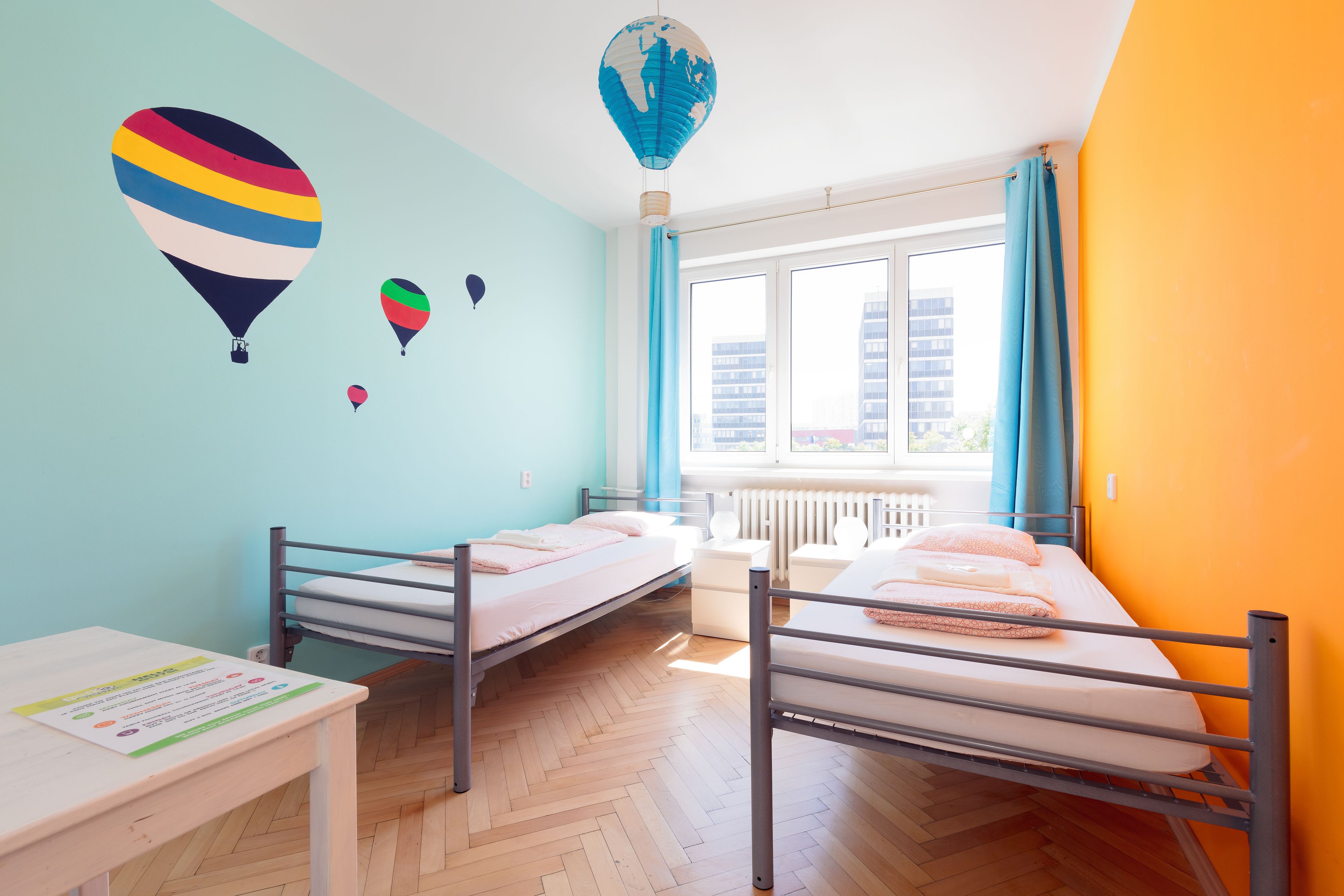 A room with two beds, a window with curtains, and a radiator.
